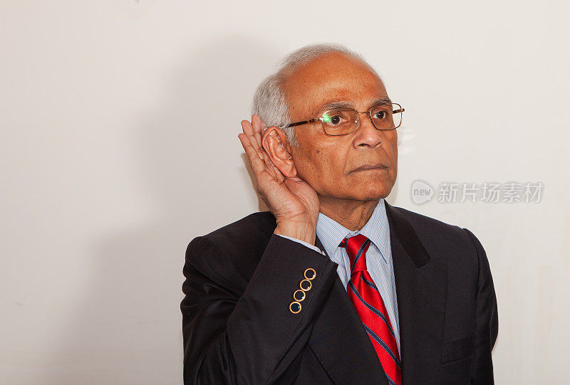 听力困难- 71岁亚洲男性用助听器将手指托向右耳表明有听力障碍